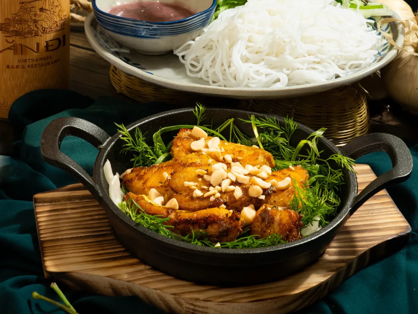Turmeric fish with dill and peanuts in a cast iron pan, vermicelli noodles behind